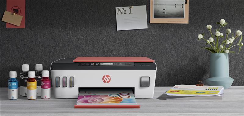 Impresora HP con sistema de tinta continua sobre un escritorio, acompañada de botellas de tinta, documentos impresos y un florero decorativo.