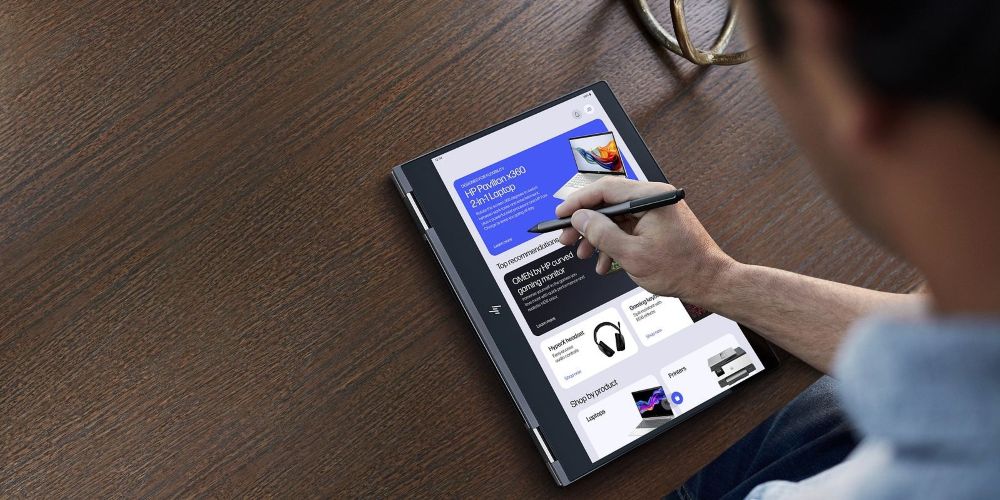 Persona usando un lápiz óptico en una laptop HP Pavilion x360 2 en 1 en modo tienda sobre un escritorio de madera