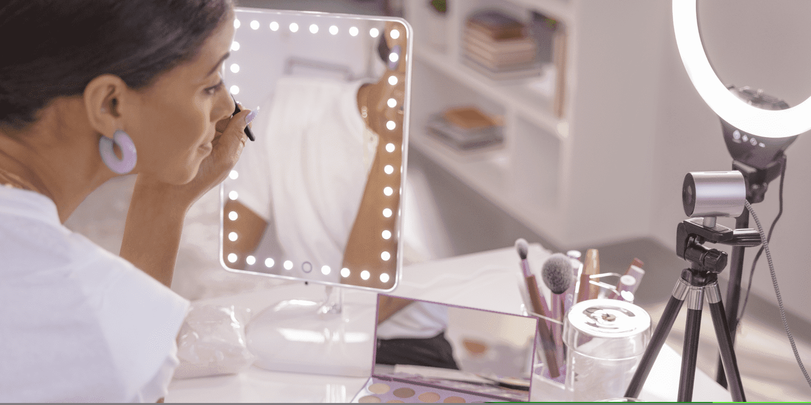 Creadora de contenido aplicando maquillaje frente a un espejo LED con webcam y anillo de luz montados en tr&iacute;pode.