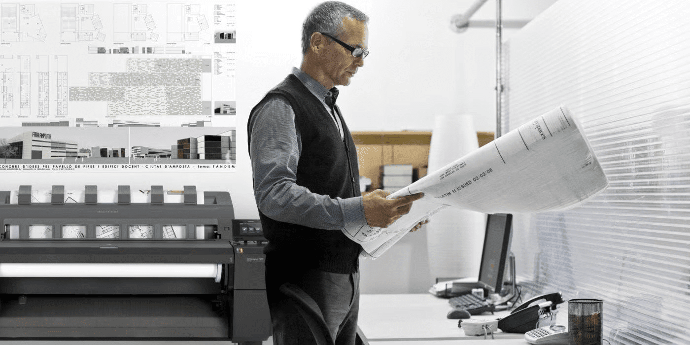 Arquitecto revisando un plano y con una impresora de gran fromato (plotter) HP al fondo. 